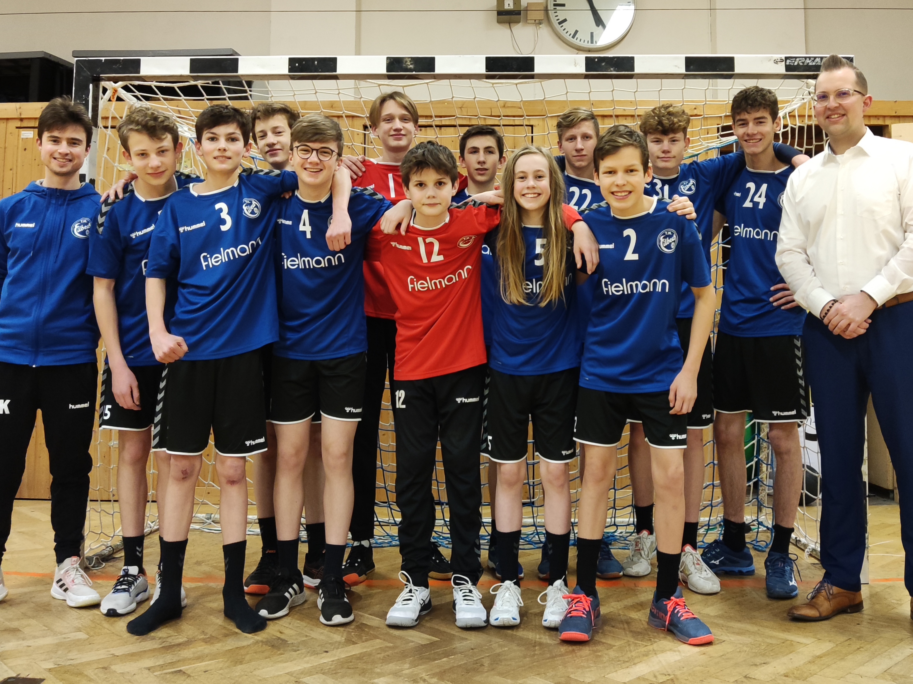 Gruppenfoto mit zwölf Jungs der MAnnschaft (männlich C1) und ihrem Trainer sowie einem jungen Mann von der Fielmann AG. Alle lächeln und stehen - teilweise Arm in Arm - zusammen.